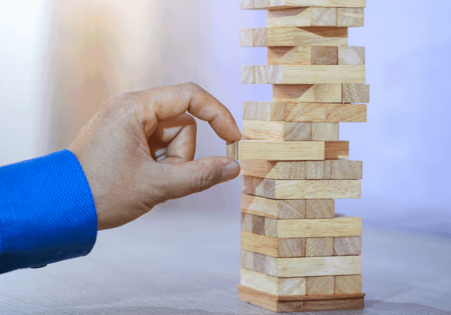 A close-up of a hand in a blue shirt carefully pulling a wooden block from a Jenga tower.