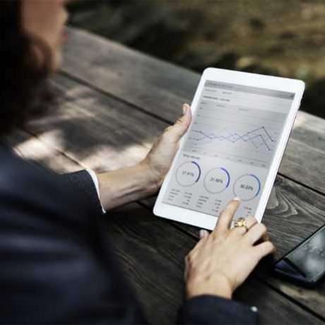 service_structure_1 Woman sitting outside on a wooden picnic table reading a report on a tablet